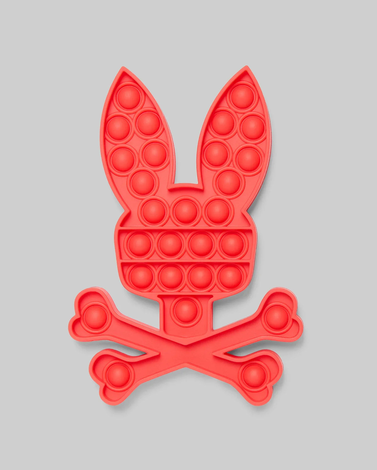 The PSYCHO BUNNY POP IT - B0A376E200 by Psycho Bunny features a red bunny head with long ears above crossed bones, resembling a fun skull-and-crossbones. Made from high-quality silicone for stress relief, set against a light gray background.