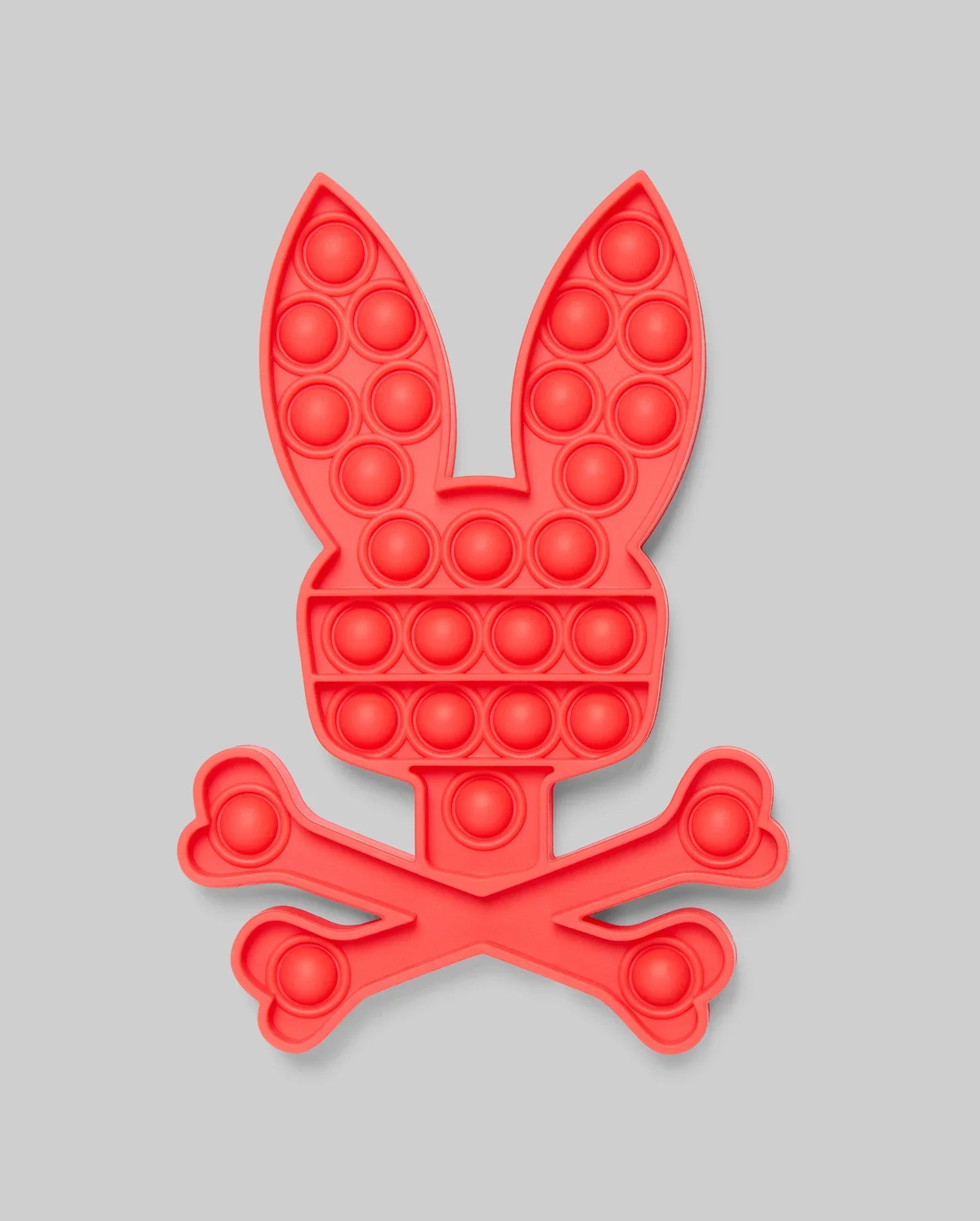 The PSYCHO BUNNY POP IT - B0A376E200 by Psycho Bunny features a red bunny head with long ears above crossed bones, resembling a fun skull-and-crossbones. Made from high-quality silicone for stress relief, set against a light gray background.