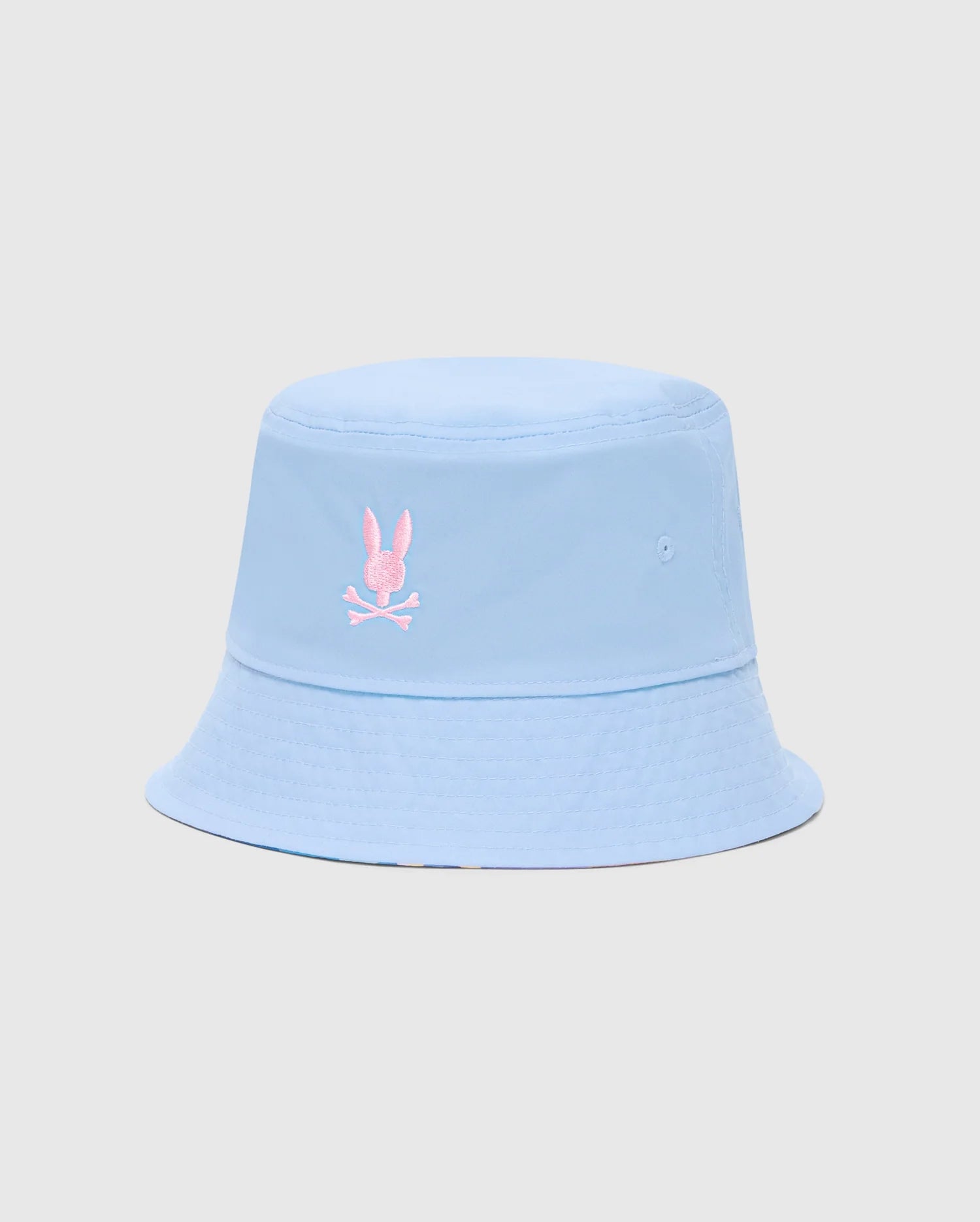 The KIDS MILOS BUCKET REVERSIBLE HAT - B0A550F200 by Psycho Bunny is light blue and embroidered with a pink rabbit head and crossbones logo on the front, displayed against a plain, light gray background.