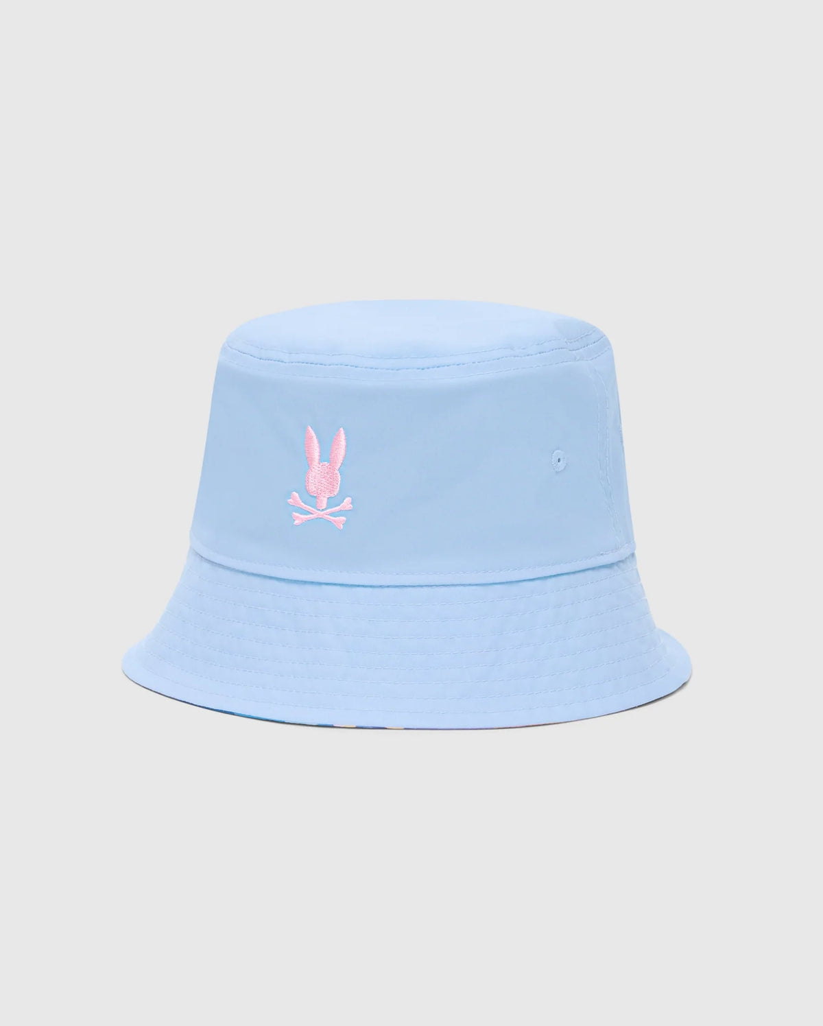 The KIDS MILOS BUCKET REVERSIBLE HAT - B0A550F200 by Psycho Bunny is light blue and embroidered with a pink rabbit head and crossbones logo on the front, displayed against a plain, light gray background.