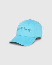The KIDS LOUISE BASEBALL CAP (B0A551C200) by Psycho Bunny features a light blue cotton twill design with a curved brim, ventilation holes, and top button. The front displays an embroidered text alongside the brand's bunny logo on a plain white background.
