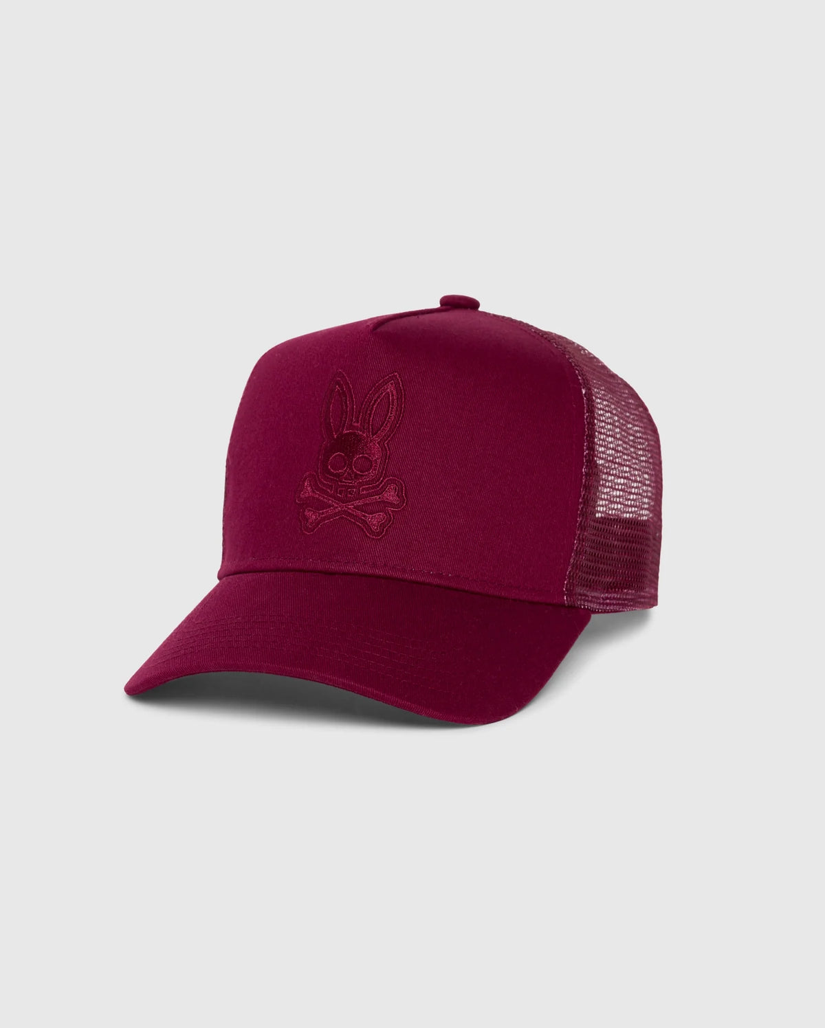 The KIDS MALTON TRUCKER CAP (B0A797D200) by Psycho Bunny is a maroon kids trucker cap with a mesh back, featuring an embroidered bunny skull and crossbones. Set against a plain gray background, its subtle design makes it an ideal accessory for an active lifestyle.