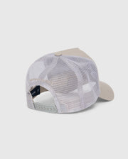 The back view of the KIDS MALTON TRUCKER CAP - B0A797D200 by Psycho Bunny showcases a beige and white design with a curved brim. The cap features a white mesh back for optimal ventilation and an adjustable snapback closure. Its front panel is solid and structured, made from cotton. The background is plain white.