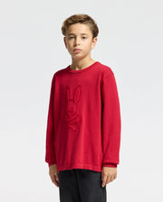 A young boy with short, light brown hair wears Psycho Bunny's KIDS COORY CHAINSTITCH COTTON SWEATER - B0E893E200 in red, showcasing a bunny logo in chainstitch embroidery on the front. He stands against a plain white background, gazing neutrally at the camera.