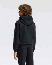 A person with curly hair, wearing a Psycho Bunny Kids Alexander Hoodie - B0H154E200 and pants, stands facing away against a plain white background.