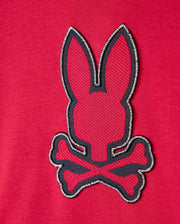 The Psycho Bunny KIDS WALTER LIGHTWEIGHT HOODIE - B0H476D200 is a red hoodie adorned with an embroidered patch showcasing a minimalist rabbit head above crossed bones, offering a modern twist on the traditional pirate skull and crossbones symbol. Made from Micro French terry fabric, it ensures ultimate comfort.