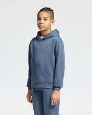 A child with braided hair is wearing a KIDS LEVY ESSENTIAL FLEECE HOODIE from Psycho Bunny, crafted entirely from cotton. Paired with matching fleece sweatpants in blue, both featuring a discreet embroidered logo on the chest, this ensemble stands out against the simple white background for a cozy and stylish look.