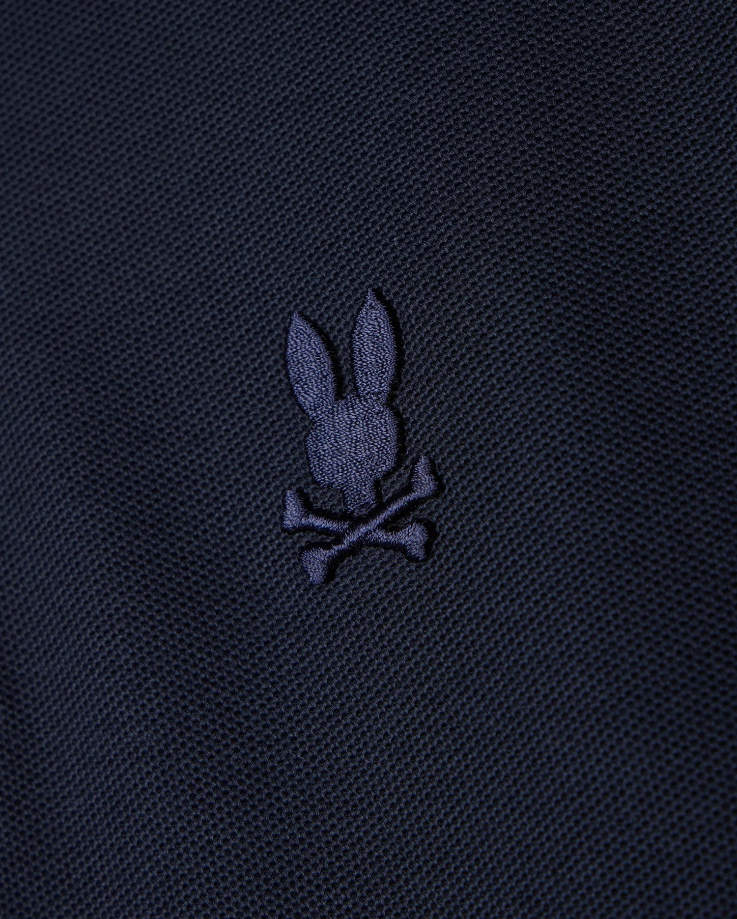 A KIDS CLASSIC PIQUE POLO SHIRT - B0K021AR00 by Psycho Bunny, featuring a dark fabric design with an embroidered chest Bunny logo depicting a bunny head and crossbones in a slightly lighter shade.