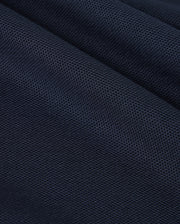 A close-up of a dark blue textured fabric reveals the fine woven pattern and small perforations characteristic of Pima cotton, similar to what's found in a Psycho Bunny KIDS CLASSIC PIQUE POLO SHIRT - B0K021AR00. The slightly folded material creates subtle shadows and highlights across its surface, reminiscent of a classic polo.