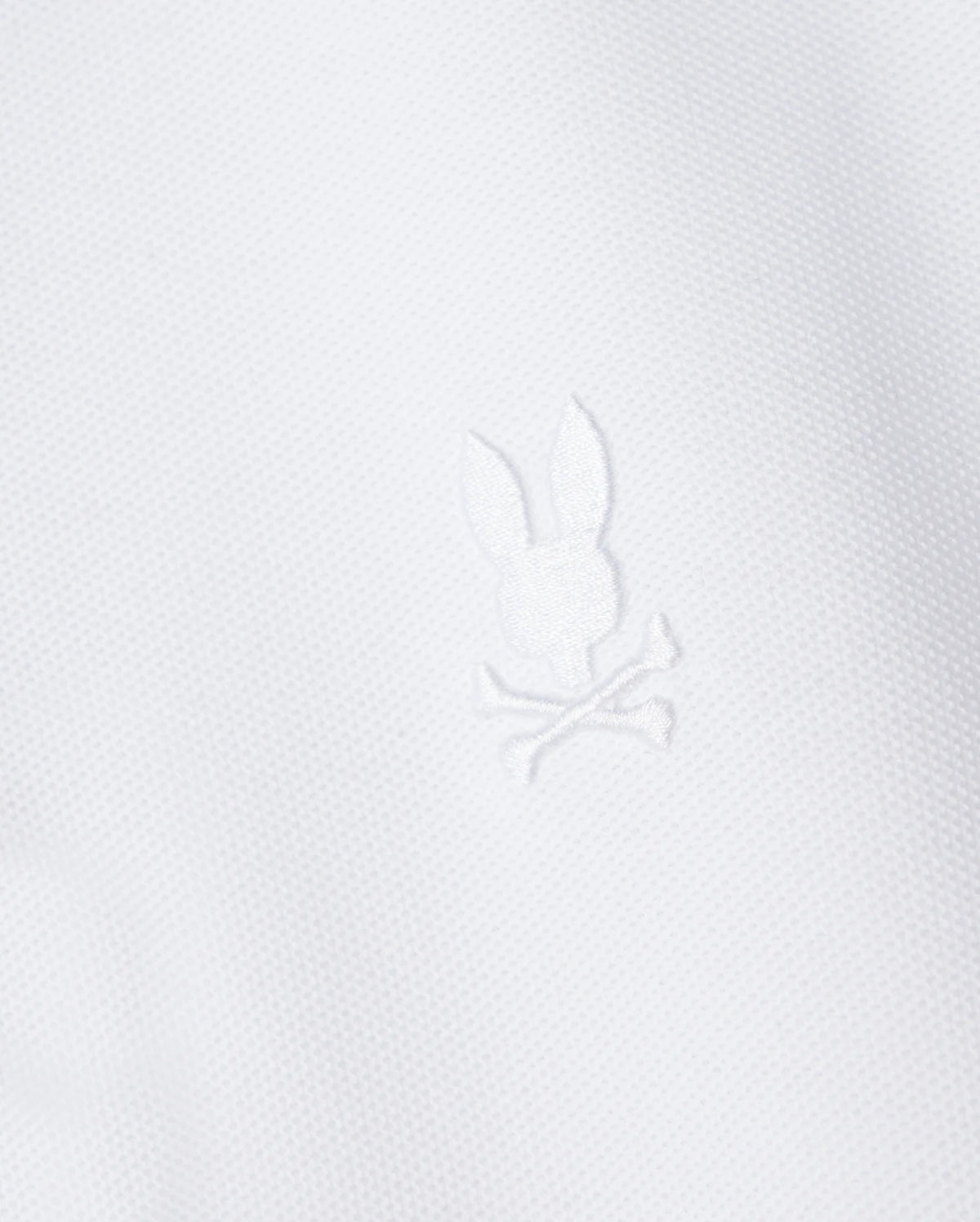 The Psycho Bunny Kids Classic Pique Polo Shirt (B0K021AR00) features a white fabric with a central embroidered Bunny motif above crossed bones, crafted in textured Pima cotton for a minimalist yet elegant design reminiscent of classic polo styles.