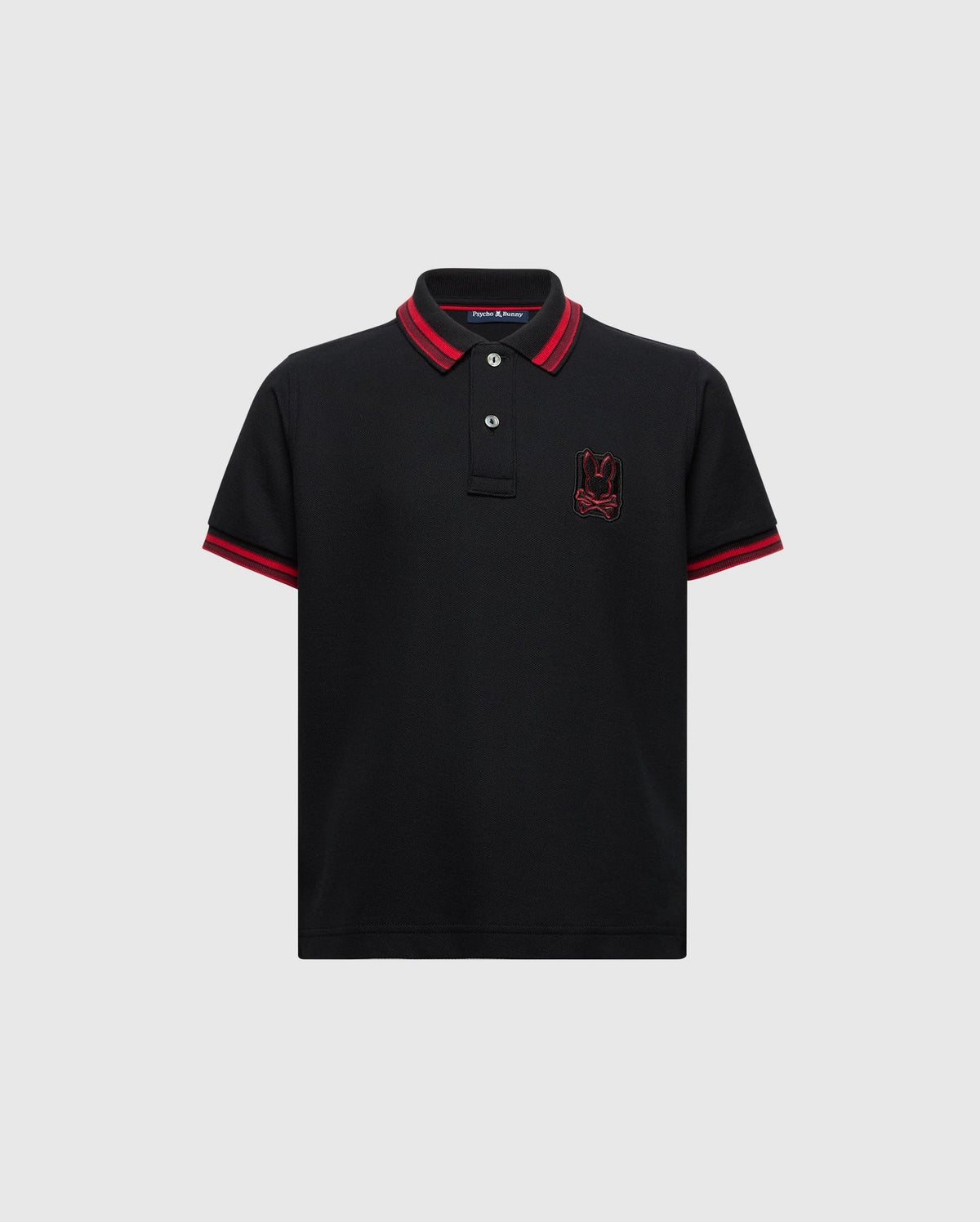 The KIDS PIERCE PIQUE POLO - B0K201E200 by Psycho Bunny is made from premium Pima cotton and features a timeless design with short sleeves. It includes red trim on the collar and sleeve hems, buttons near the collar, and an embroidered red bunny logo on the left chest.