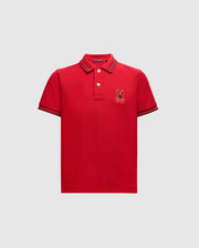 Introducing the KIDS PIERCE PIQUE POLO - B0K201E200 by Psycho Bunny: This stylish red polo shirt for kids is made from premium Pima cotton. It features a classic collar and button placket, along with a small embroidered Bunny logo on the left side of the chest. The sleeves and collar are accented with thin, contrasting stripes set against a light gray background, adding a touch of sophistication to this trendy piece.