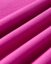 Close-up view of the vibrant pink Pima cotton piqué fabric, featuring a textured, woven pattern from the KIDS RIVIERA PIQUE POLO SHIRT by Psycho Bunny. The fabric is folded into several soft ridges, emphasizing its smooth and structured appearance.