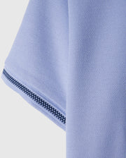 Close-up of a textured light blue fabric, possibly the sleeve of the Psycho Bunny Kids Riviera Pique Polo Shirt (B0K640C200), featuring a black and white striped trim along the edge.