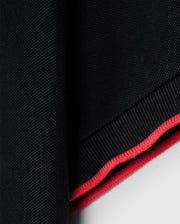 Close-up of a navy blue fabric from the KIDS KAYDEN PIQUE POLO - B0K675C200 by Psycho Bunny, featuring bold contrasting stripes in red and pink along the edge. The texture resembles Pima cotton piqué, giving it a coarse, knit-like appearance. The neat border sharply contrasts with the solid navy blue color, reminiscent of the classic Kayden pique polo design.