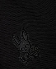 Close-up of a black Pima cotton piqué fabric with an embroidered Psycho Bunny logo on the KIDS MALTON PIQUE POLO SHIRT - B0K950D200: featuring a skull with elongated bunny ears above two crossed bones, all in a matching black color.