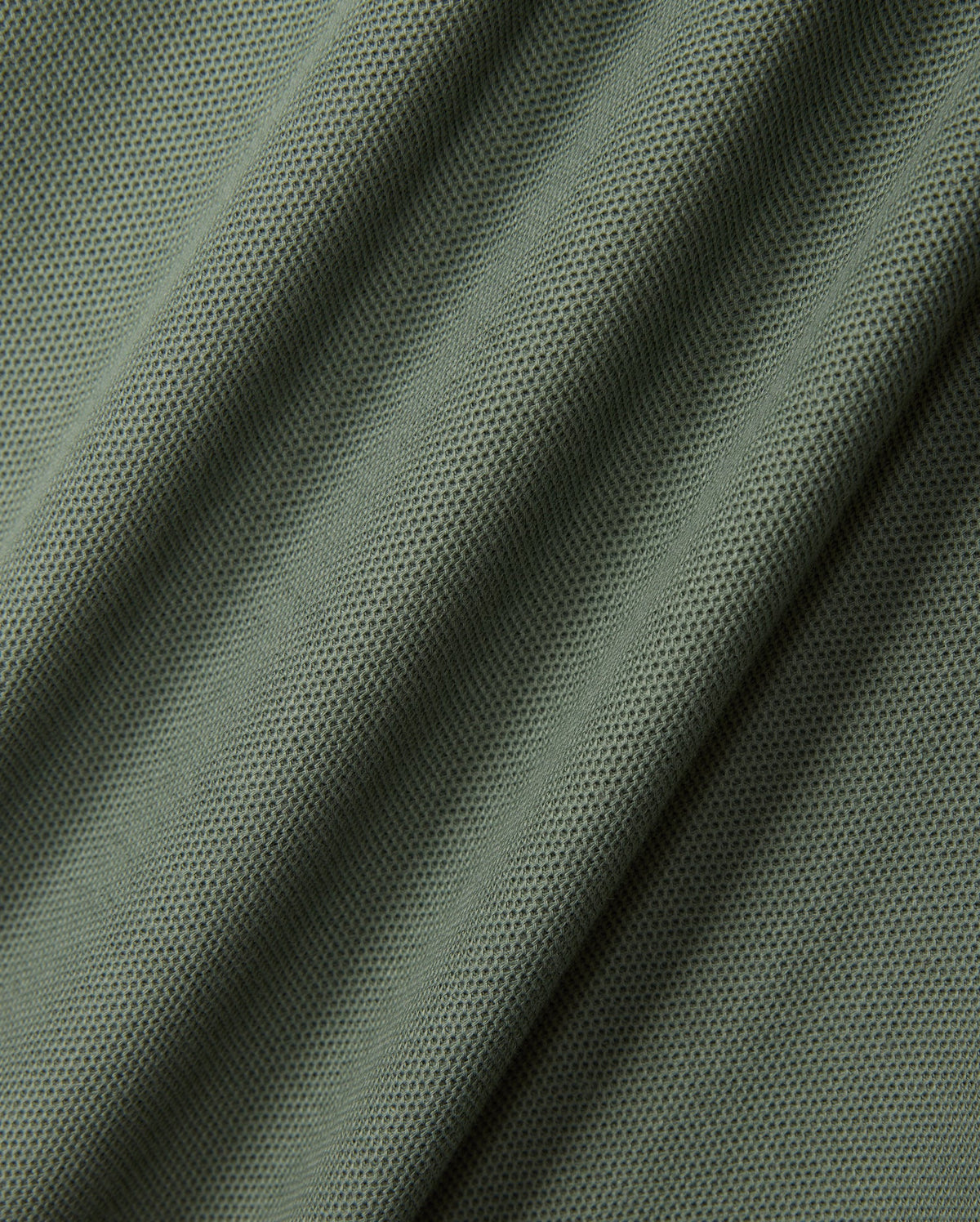Close-up of green fabric with a mesh-like pattern, featuring diagonal folds and a textured surface that evokes the fine weave of the diamond piqué-patterned cuffs on the KIDS MALTON PIQUE POLO SHIRT by Psycho Bunny.