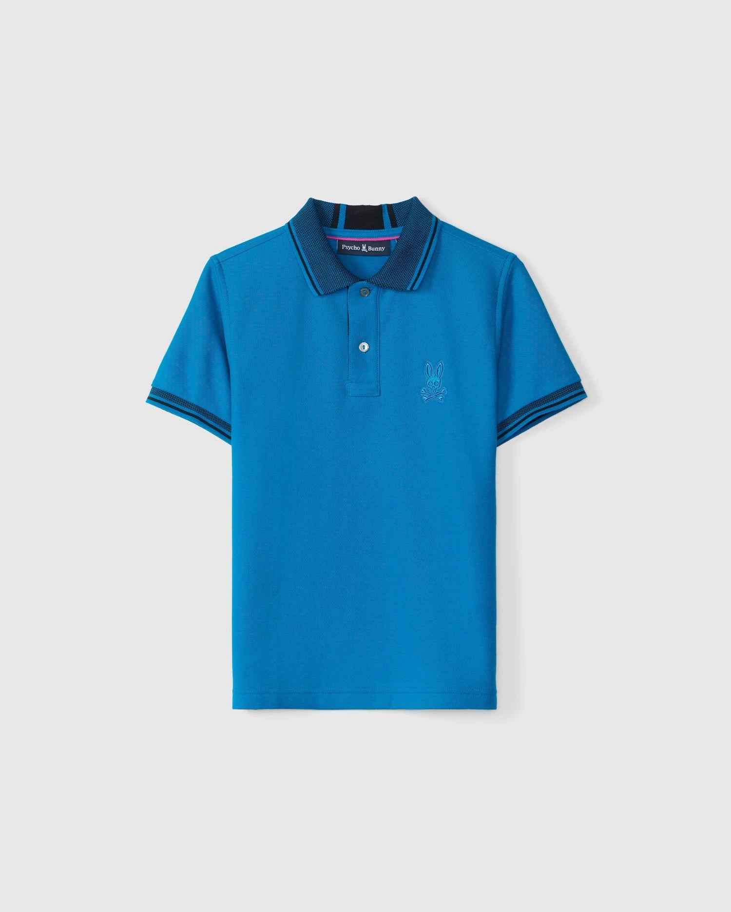 The KIDS MALTON PIQUE POLO SHIRT - B0K950D200 from Psycho Bunny is a bright blue polo shirt made from Pima cotton piqué. It includes a collar, two mother-of-pearl buttons, and a subtle embroidered bunny logo on the left chest. The design features navy blue and white stripes on the collar and sleeve edges against a plain gray background.