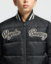 A boy wears the KIDS FRASER FASHION PUFFER - B0N338E200 from Psycho Bunny, a trendy black puffer jacket with white embroidered text "Psycho Bunny" on the front. This warm kids' fashion piece, featuring a ribbed collar, keeps him cozy. His face is partially visible against a plain background.