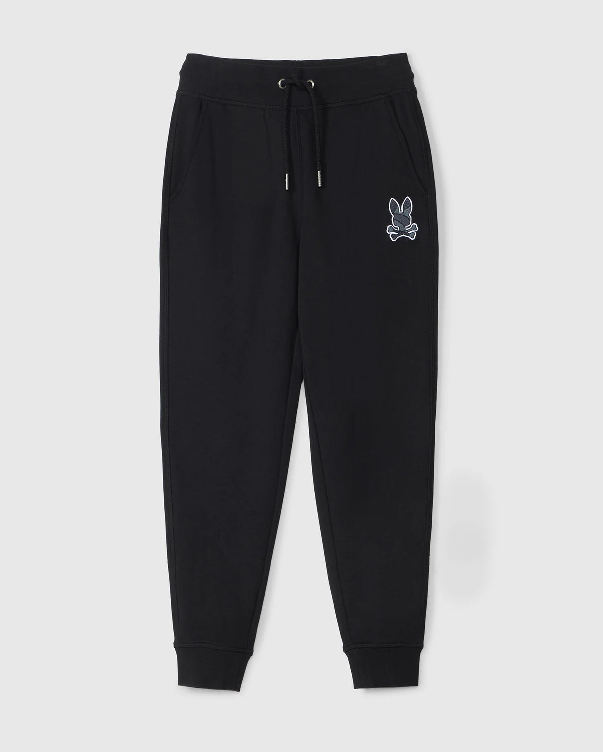 The KIDS LENOX REGULAR FIT SWEATPANT by Psycho Bunny is a pair of black jogger pants with an elastic waistband, drawstring, and ribbed ankle cuffs. These kids' sweatpants also feature a white embroidered graphic of a rabbit head above crossed bones on the left pocket.