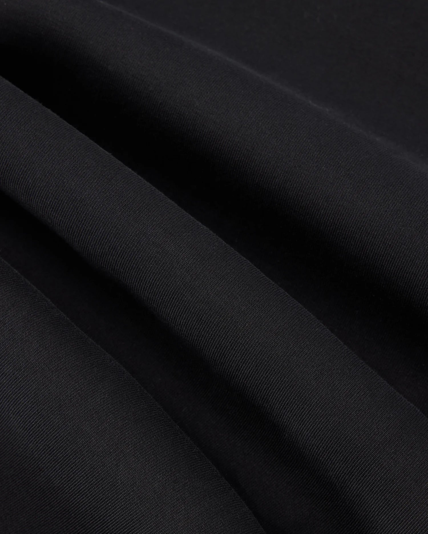 Close-up image of the black fabric with fine, parallel ribbing showcasing its texture. The fabric exhibits slight waves due to gentle folds, reminiscent of the subtle detail found in the high-quality KIDS TRAVIS TRACK PANT - B0P143D200 by Psycho Bunny, which is both elastic and comfortable.