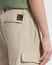 Someone wearing KIDS GREEN VALLEY CARGO PANT - B0P199E200 by Psycho Bunny, featuring an orange and black patch with a stylized rabbit and text on the back pocket. These comfortable-fit pants have side pockets, highlighting their rear design.