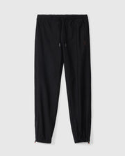 A pair of Psycho Bunny Kids Madison Commuter Pants (B0P395Z1WB) in black, featuring elastic cuffs, a drawstring waistband, and a small embroidered logo on the left thigh. These joggers offer a relaxed fit and include zippered expansion vents, displayed against a plain white background.