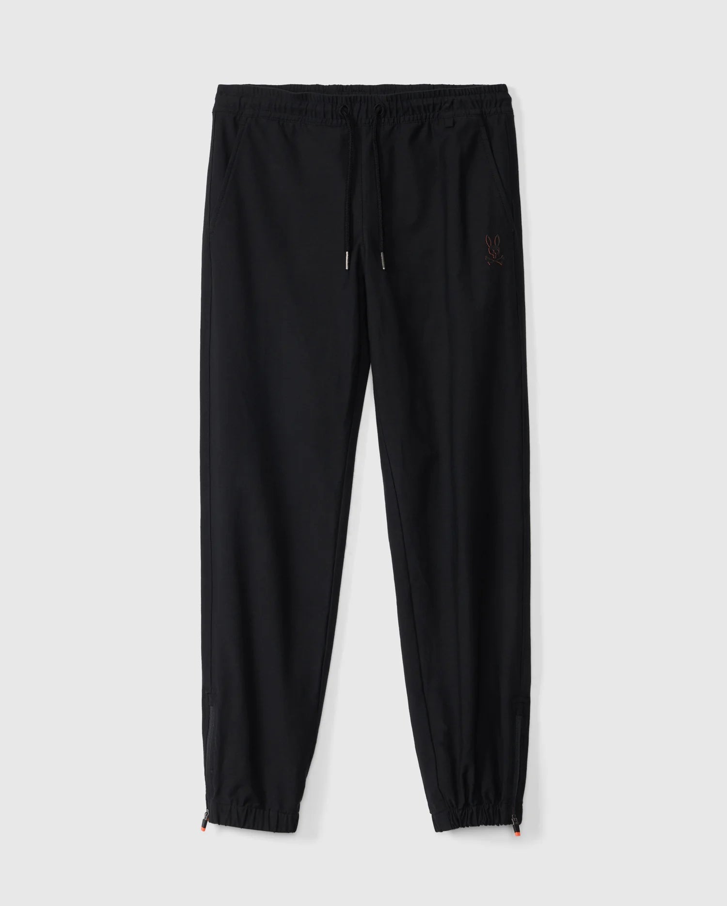 A pair of Psycho Bunny Kids Madison Commuter Pants (B0P395Z1WB) in black, featuring elastic cuffs, a drawstring waistband, and a small embroidered logo on the left thigh. These joggers offer a relaxed fit and include zippered expansion vents, displayed against a plain white background.