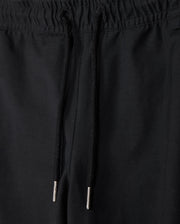 A close-up image of the black KIDS MADISON COMMUTER PANT - B0P395Z1WB by Psycho Bunny, focusing on the waistband. The pants feature an elastic waistband with drawstrings that have metal tips. The fabric appears to be smooth and solid in color.