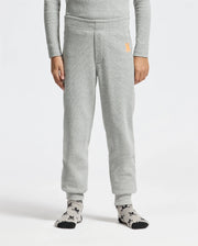 A person is comfortably standing, wearing the gray KIDS VAL WAFFLE PANT - B0P673E200 by Psycho Bunny, featuring a small orange logo near the pocket. They also have on a gray long-sleeve shirt and gray socks with a black pattern against a plain white background.