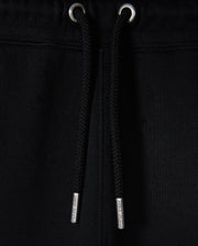 Close-up of black Psycho Bunny KIDS MONROE TWILL PATCH FLEECE SWEATPANT with luxury finishes, including drawstrings with metal tips threaded through metal eyelets at the waistband against a black fabric backdrop.