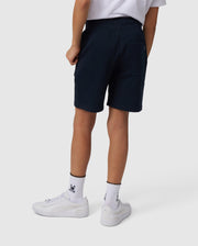 The person, embodying an active lifestyle, wears a white t-shirt and black shorts similar to Psycho Bunny's KIDS LENOX SWEATSHORT - B0R377B200. They complete the look with rabbit-logo white socks and white sneakers, standing against a plain backdrop, ready for movement and adventure.