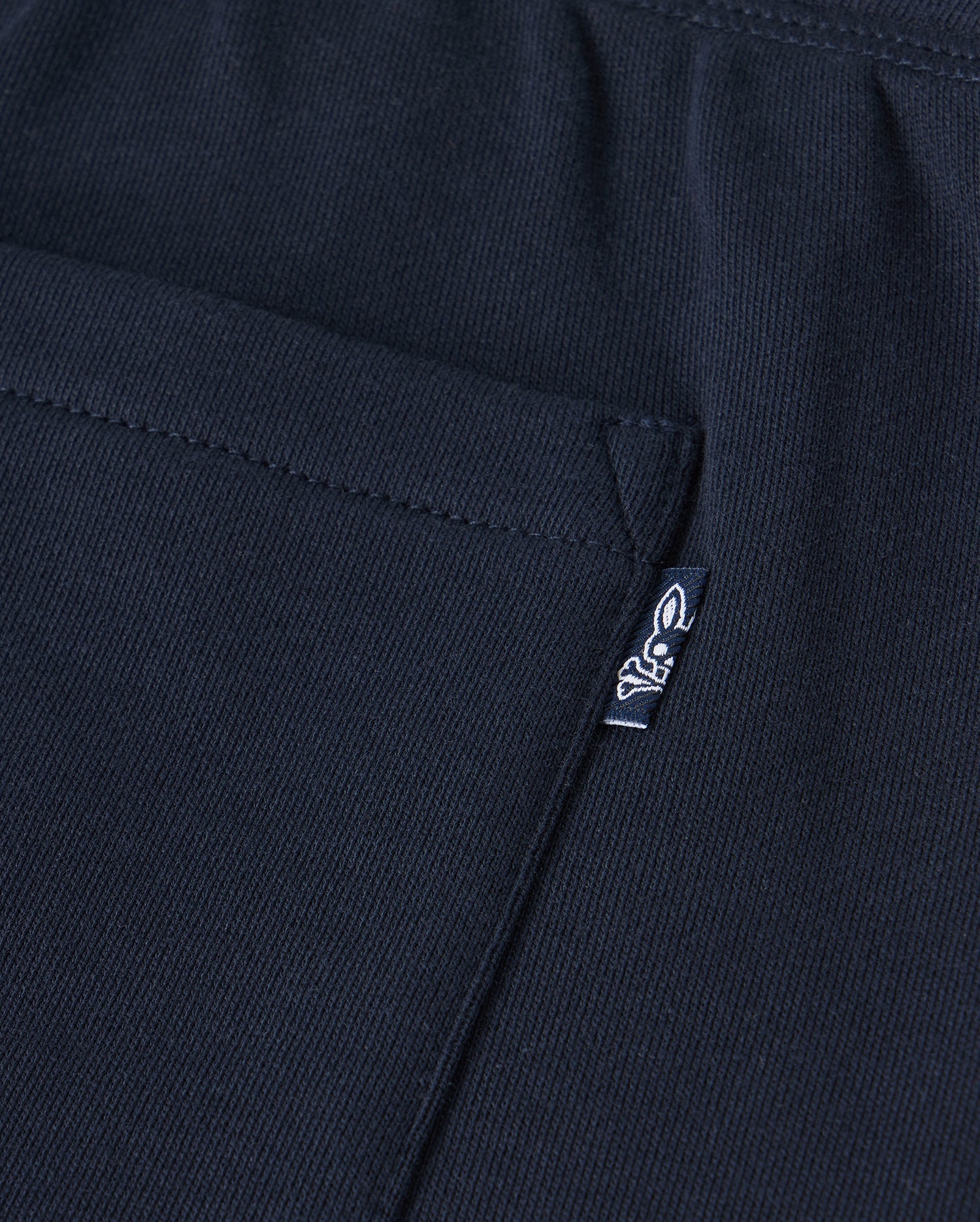 Close-up of a black Psycho Bunny Kids Lenox Sweatshort B0R377B200 in breathable fleece, featuring a pocket and small white logo tag with stylized animal figure on ribbed fabric—ideal for active kids.