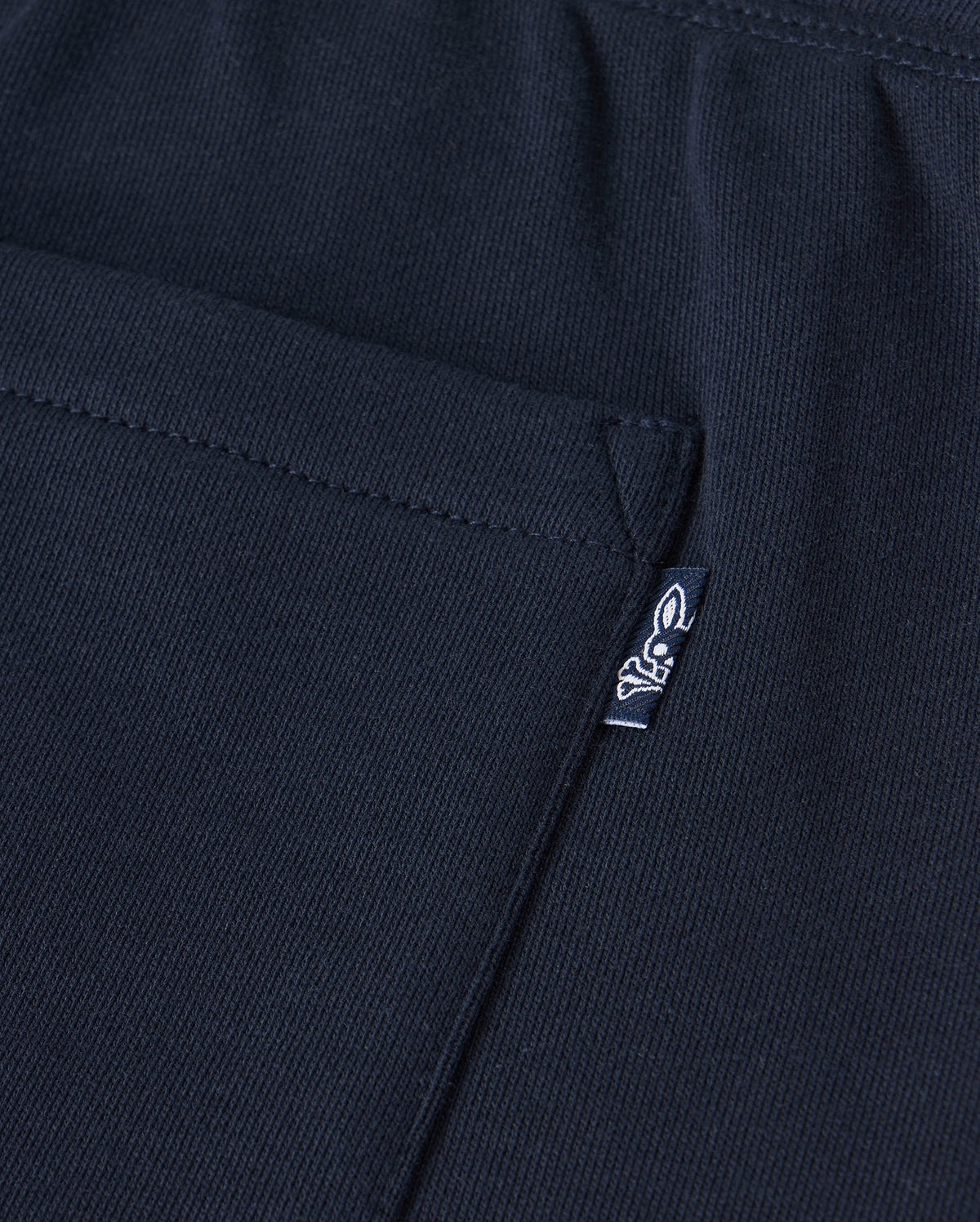 Close-up of a black Psycho Bunny Kids Lenox Sweatshort B0R377B200 in breathable fleece, featuring a pocket and small white logo tag with stylized animal figure on ribbed fabric—ideal for active kids.