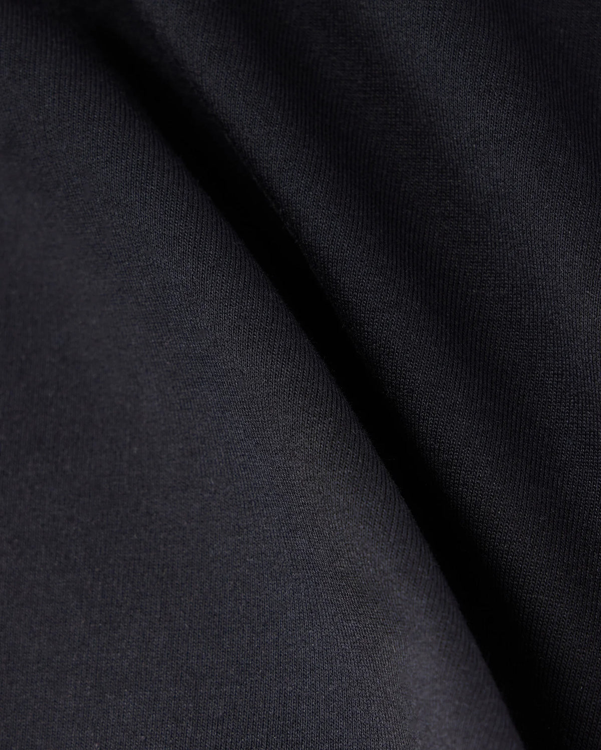 Close-up of a smooth, dark fabric with soft folds, displaying a gradient of black and dark gray shades. The texture appears uniform and slightly matte, creating subtle shadows and highlights across the surface. This Micro French Terry fabric promises both comfort and style in every Psycho Bunny KIDS LIVINGSTON TERRY SWEATSHORT - B0R408B200 design.