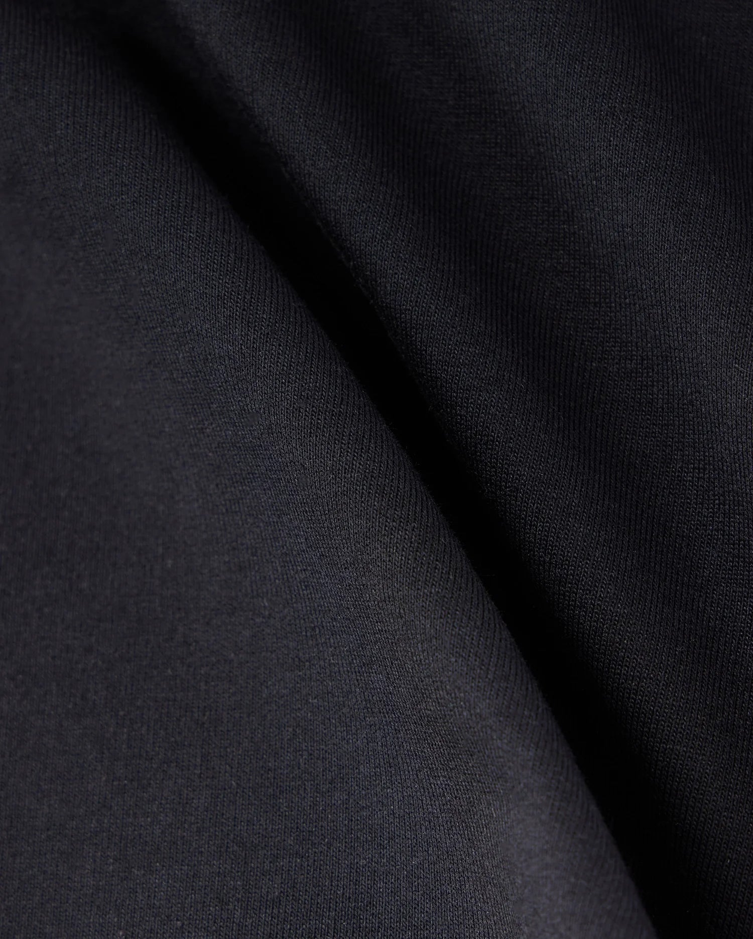 Close-up of a smooth, dark fabric with soft folds, displaying a gradient of black and dark gray shades. The texture appears uniform and slightly matte, creating subtle shadows and highlights across the surface. This Micro French Terry fabric promises both comfort and style in every Psycho Bunny KIDS LIVINGSTON TERRY SWEATSHORT - B0R408B200 design.