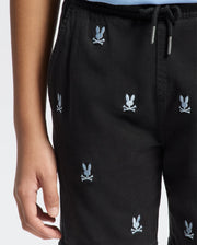A person is wearing Psycho Bunny’s KIDS ALL OVER WILLIS STRETCH TENCEL SHORT (B0R559F200) with a black base featuring a light blue bunny and crossed bones pattern. These regular-fit shorts are made from Stretch Tencel™ and have a drawstring waist, set against a plain white background.