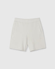 A pair of light gray, knee-length kids casual shorts with an elastic waistband and two side pockets. Made from a soft stretch modal-cotton-blend jersey, these Psycho Bunny KIDS LYONS SWEATSHORT - B0R578C200 feature a subtle embroidered design near the bottom of the left leg depicting a small bunny outline. Displayed against a plain white background.