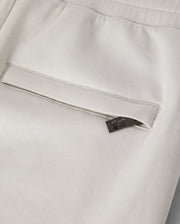 Close-up of the back pocket of a pair of light-colored KIDS LYONS SWEATSHORT - B0R578C200, featuring a small black tag with a subtle design peeking out from the pocket. Made from soft stretch modal-cotton-blend jersey, the fabric appears smooth and slightly elastic. The sweatshorts have a clean and modern look. Psycho Bunny promotes both style and comfort in this garment designed for active kids.