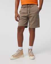 A person is standing against a plain background, wearing an orange shirt, KIDS FRENCH TERRY SHORTS - B0R829ARFT by Psycho Bunny with a small embroidered emblem on the left leg, white socks, and tan high-top sneakers with white laces.