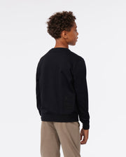 A young boy wearing a dark blue Psycho Bunny KIDS FRENCH TERRY SWEATSHIRT - B0S830ARFT and beige pants, seen from the back, with a focus on the embroidered bunny logo detail on the sweatshirt.