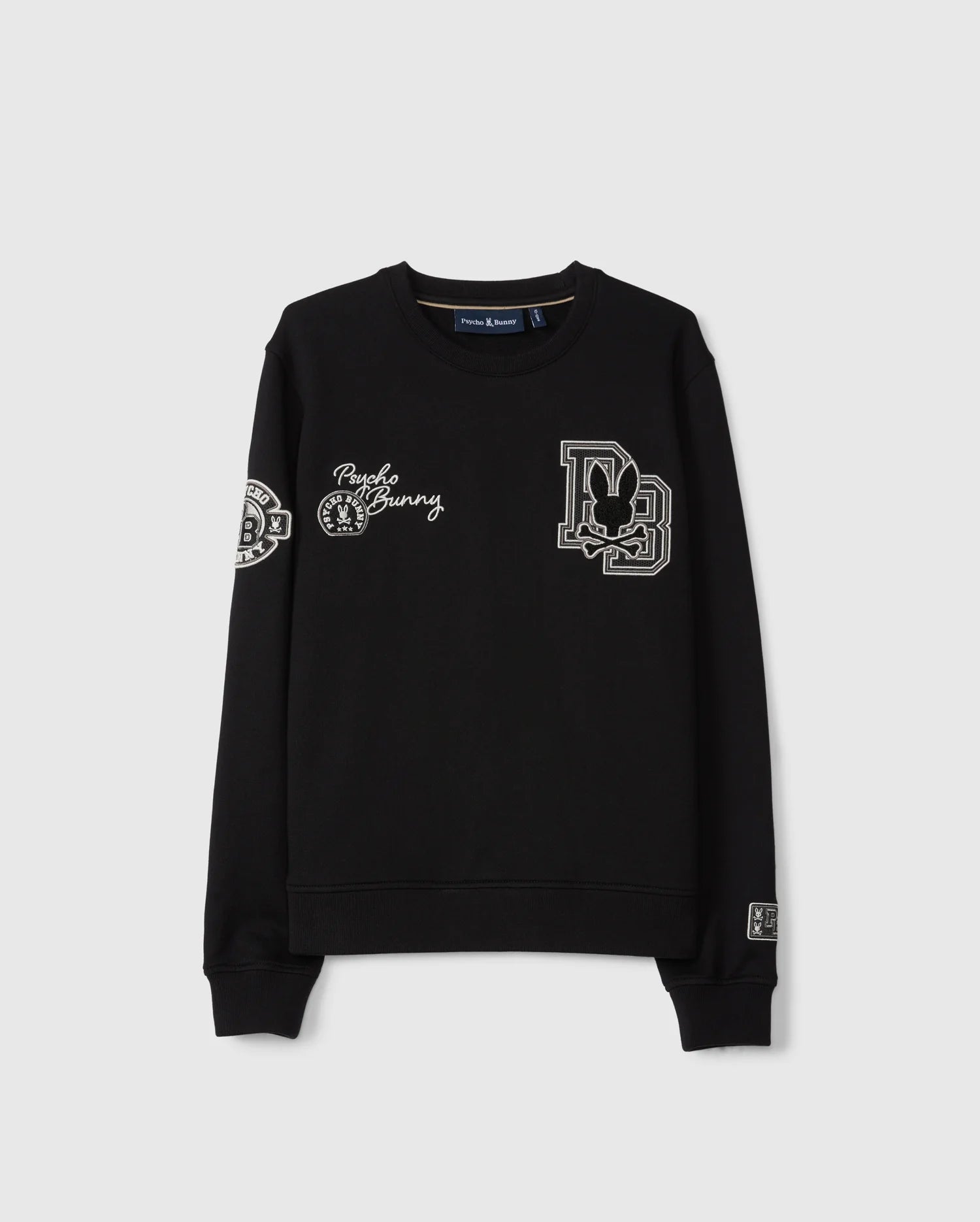 The KIDS ZACK VARSITY SWEATSHIRT by Psycho Bunny features chenille embroidery with a stylized letter “D” containing a rabbit, "Punk Bunny," and various decorative patches on the chest and sleeves. Its vintage-inspired logo is highlighted against the plain gray background of this black varsity sweatshirt.