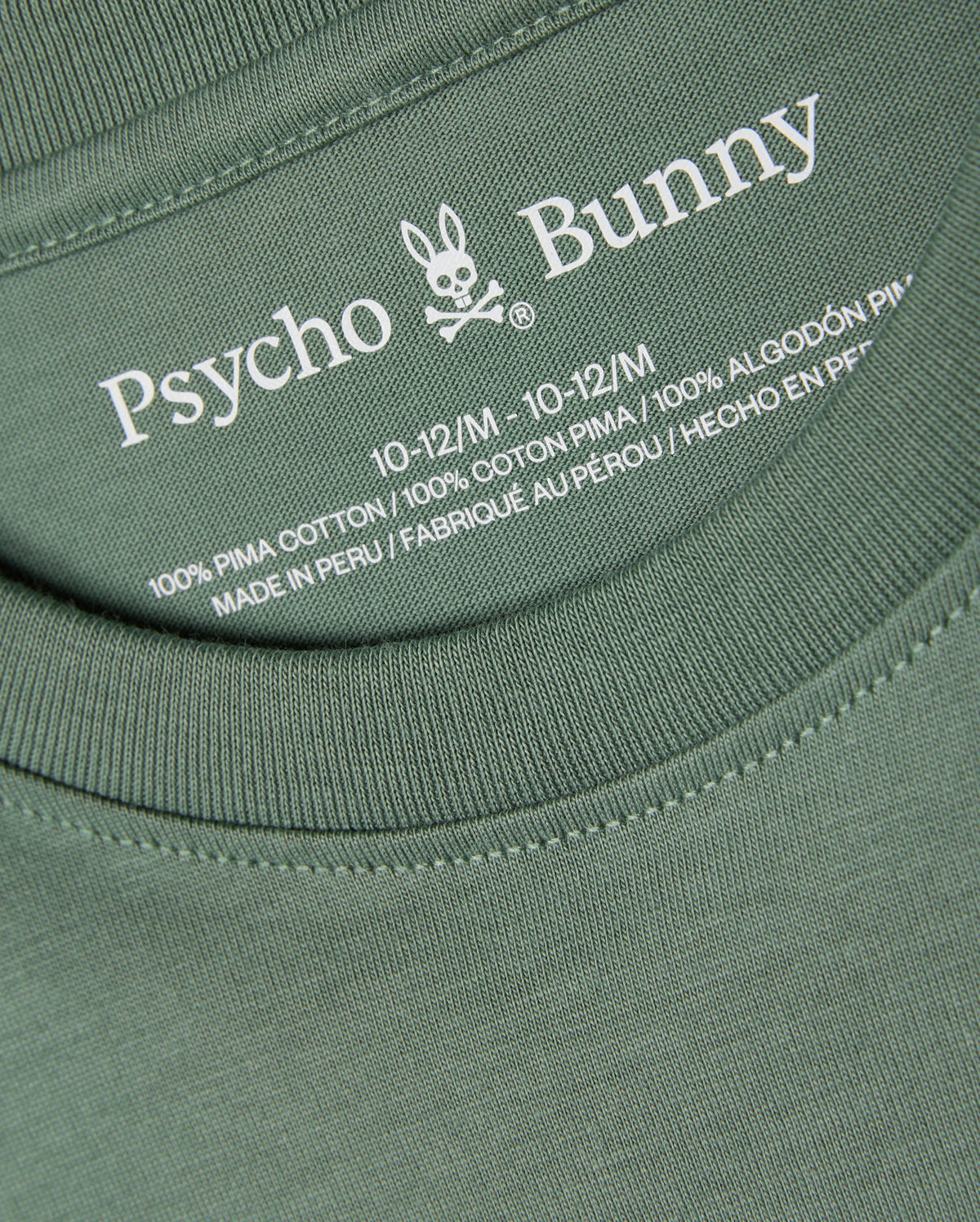 Close-up of the KIDS ALBERTON LONG SLEEVE TEE - B0T867D200 in green, featuring the label with the brand name "Psycho Bunny" and its signature bunny logo. Made from 100% Pima cotton and crafted in Peru, this versatile layering piece comes in size 10-12/M.