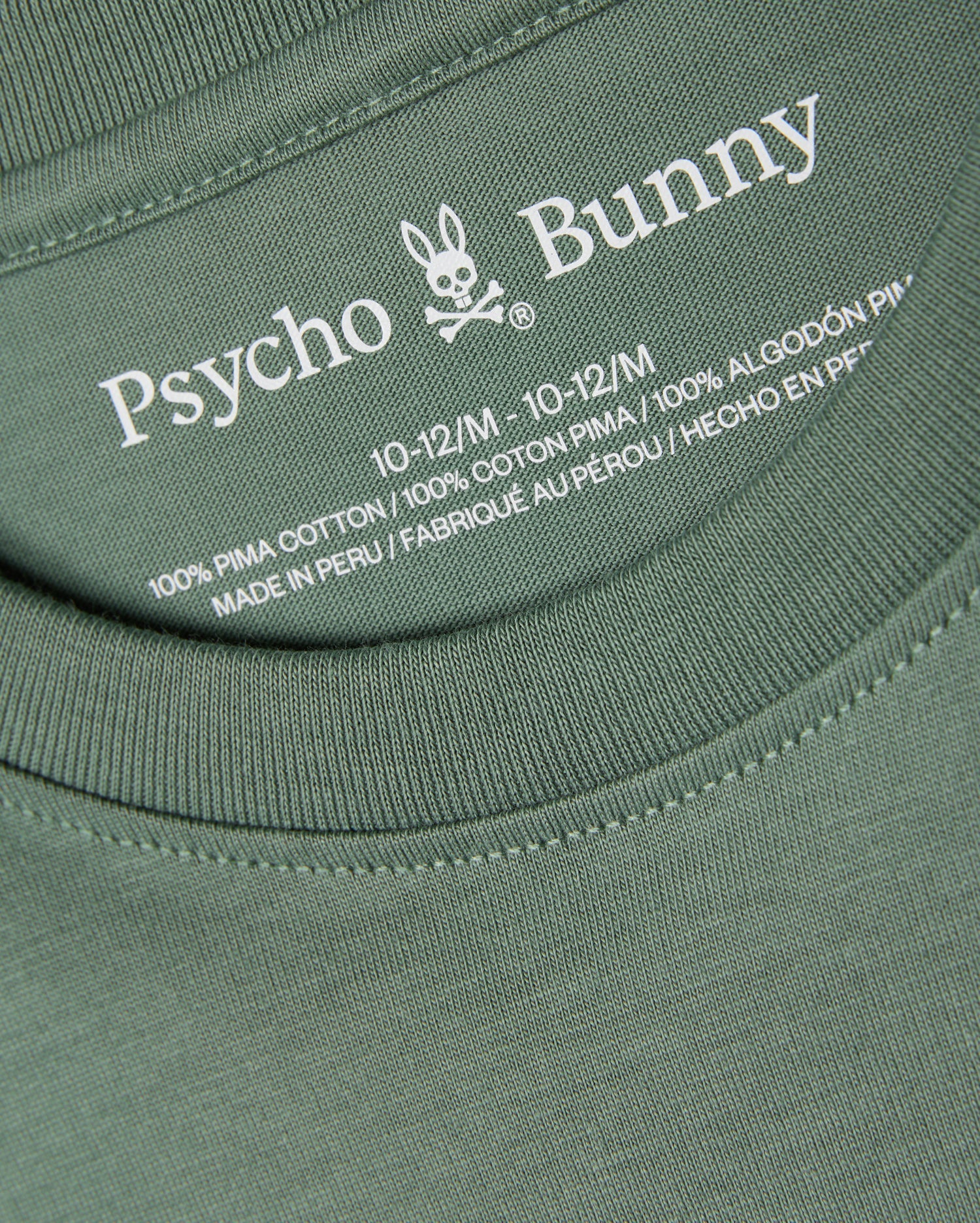Close-up of the KIDS ALBERTON LONG SLEEVE TEE - B0T867D200 in green, featuring the label with the brand name "Psycho Bunny" and its signature bunny logo. Made from 100% Pima cotton and crafted in Peru, this versatile layering piece comes in size 10-12/M.