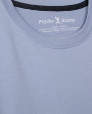 Close-up of the KIDS MONROE LONG SLEEVE TEE by Psycho Bunny, in light blue with logo and brand name on the inside collar. Made from pima cotton for a soft feel, it features cozy stitching details and texture, offering a regular fit that embodies versatile style. Model: B0T975D200.