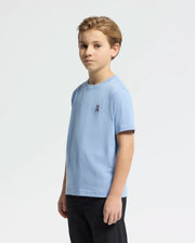 A young boy with short, light brown hair is wearing Psycho Bunny's KIDS CLASSIC CREW NECK TEE (B0U014B200) in light blue Pima cotton with an embroidered Bunny logo on the chest. He pairs it with black pants, standing against a white background and looking slightly to the right.