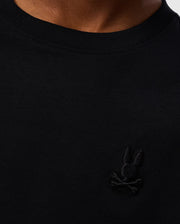 Close-up of the upper chest area of a person wearing a Psycho Bunny KIDS EMBROIDERED CLASSIC TEE - B0U020AR00 made from Peruvian Pima cotton. The logo is a black silhouette of a rabbit's head with crossbones underneath it. The background is white, and the image focuses on the details of this timeless silhouette.