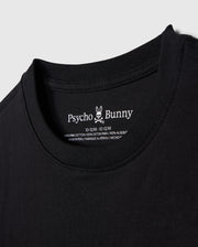 Close-up image of a black T-shirt neckline with a label showing the brand name "Psycho Bunny" alongside its bunny logo, and the size 10-12 M. The KIDS EMBROIDERED CLASSIC TEE - B0U020AR00 is made of 100% Peruvian Pima cotton, ensuring ultimate comfort and quality. This piece showcases a timeless silhouette and is proudly made in Peru.