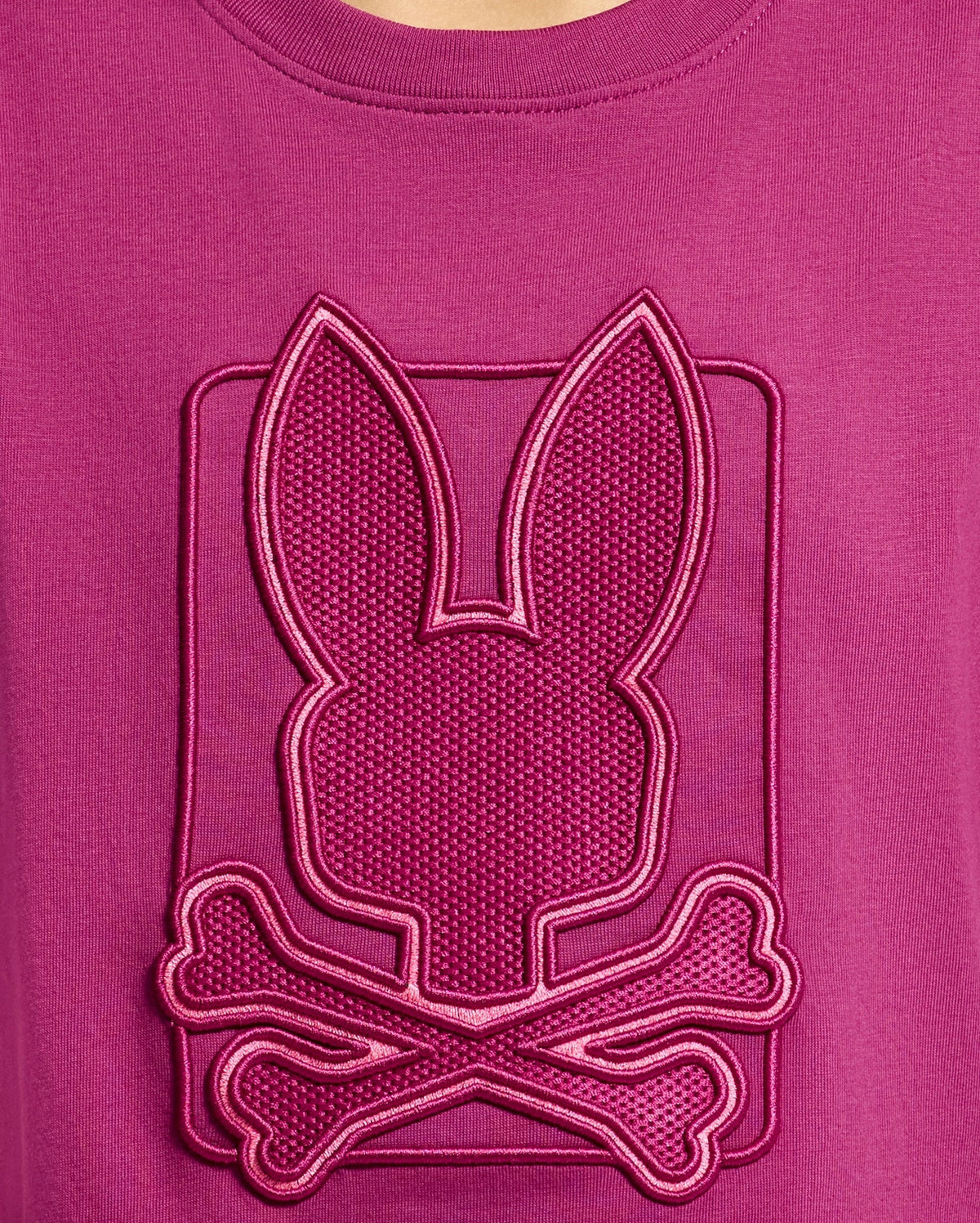 The KIDS PIERCE GRAPHIC TEE - B0U115E200 by Psycho Bunny features a magenta Pima cotton design adorned with a textured emblem. The emblem showcases a stylized bunny graphic above crossed bones, complete with an embroidered design and raised border for a striking three-dimensional effect—perfect for kids who enjoy playful details!