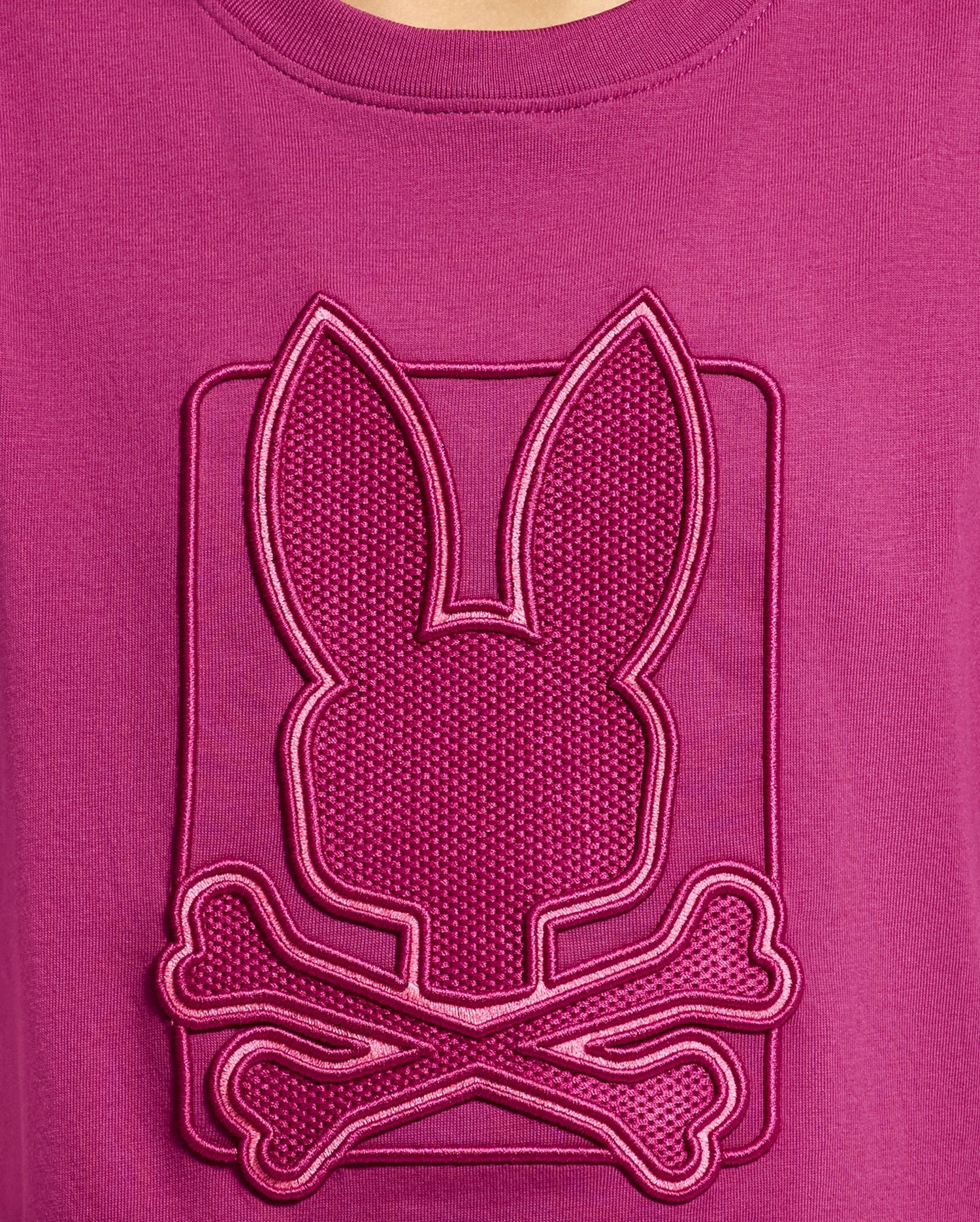 The KIDS PIERCE GRAPHIC TEE - B0U115E200 by Psycho Bunny features a magenta Pima cotton design adorned with a textured emblem. The emblem showcases a stylized bunny graphic above crossed bones, complete with an embroidered design and raised border for a striking three-dimensional effect—perfect for kids who enjoy playful details!